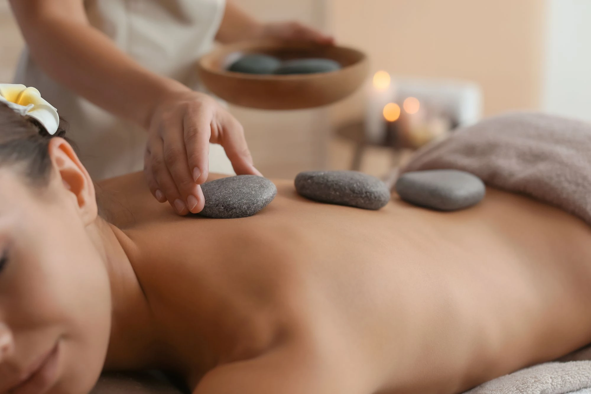 A therapist placing a hot stone on the back of a client lying face down during a beauty treatment.