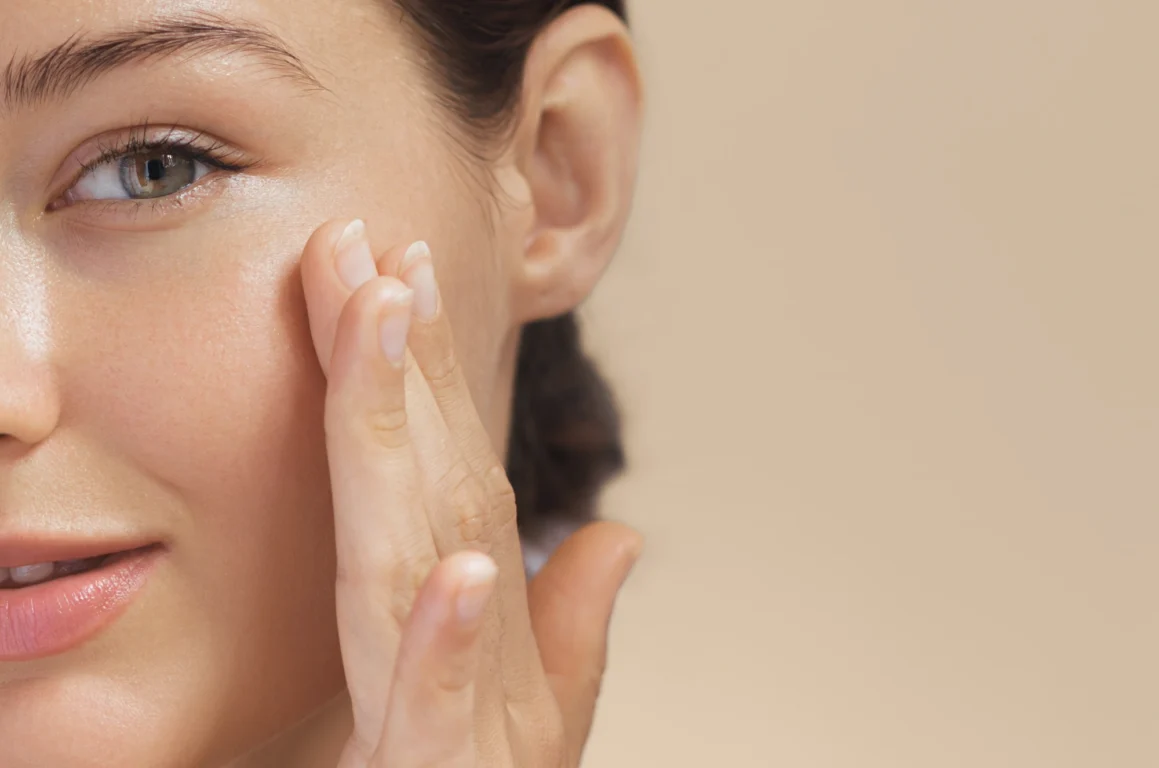 Woman touches glowing skin on her face, admiring results from recent HydraFacial. 