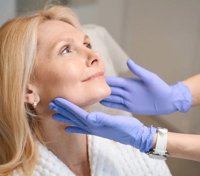 A woman in a robe being prepared for treatment by a beauty therapist wearing blue gloves.