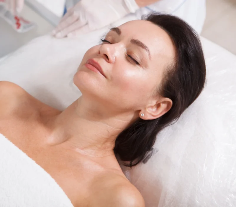 A woman with dark hair lying down for a facial treatment.