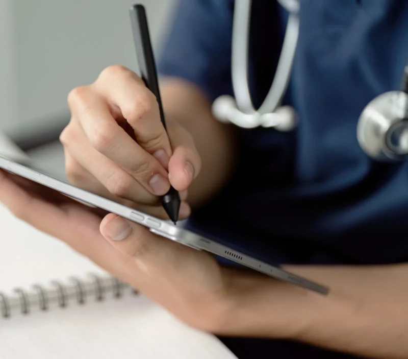 A medical professional taking notes with a tablet.
