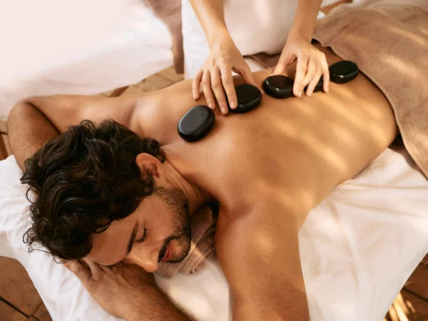 A man on a massage table receiving a hot stone massage. Hot stones are lined down the middle of his back.