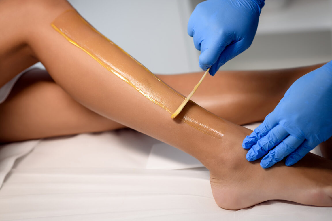 A woman has her legs waxed by a beauty therapist wearing blue gloves.